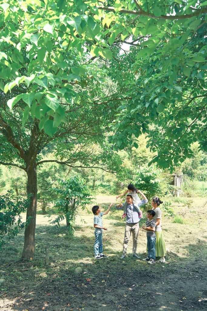 一家人在田野大樹下互動，展現溫馨真誠的田園生活。