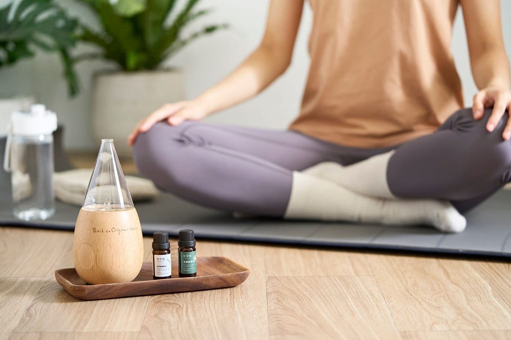 天然精油擴香儀與精油瓶置於靜坐者旁，營造放鬆療癒的品牌情境。
