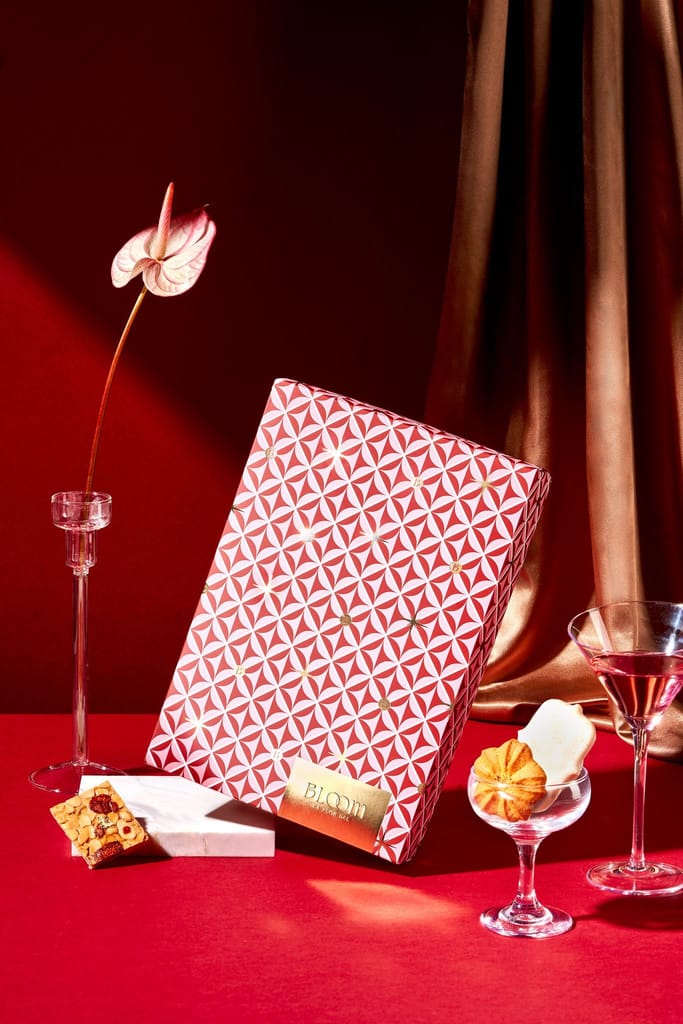 綻紅寶石新年限定禮盒的精美擺拍，紅色背景襯托著禮盒、鮮花、甜點與飲品，呈現節慶奢華感。