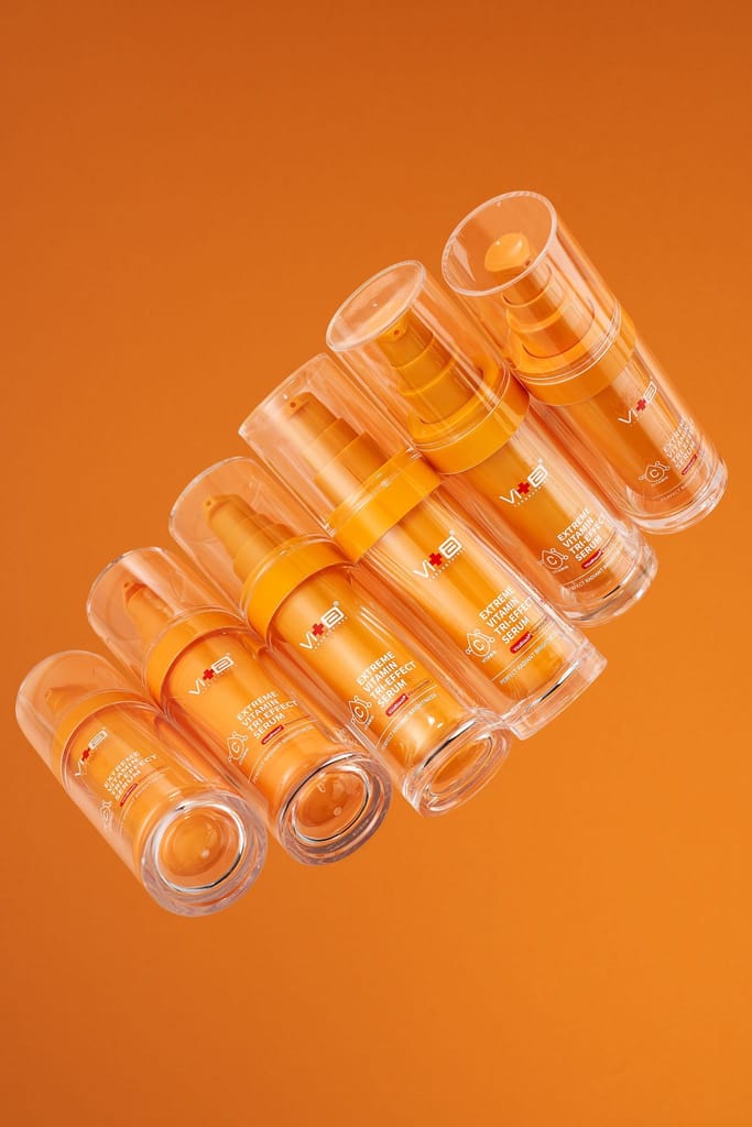 多瓶「薇佳維他命完美三抗精華」在暖橘色背景中呈現，象徵其注入光潤能量，告別肌膚暗沉蠟黃，打造透亮玻璃肌的功效。