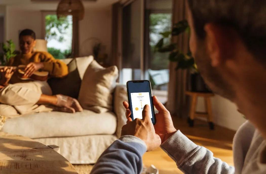 Man using phone to control Somfy taHoma app controlled motorized roller shades