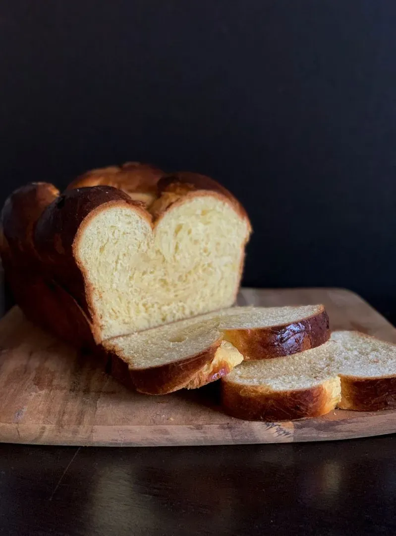 Une brioche posé sur une planche à découper en bois avec deux tranches coupées