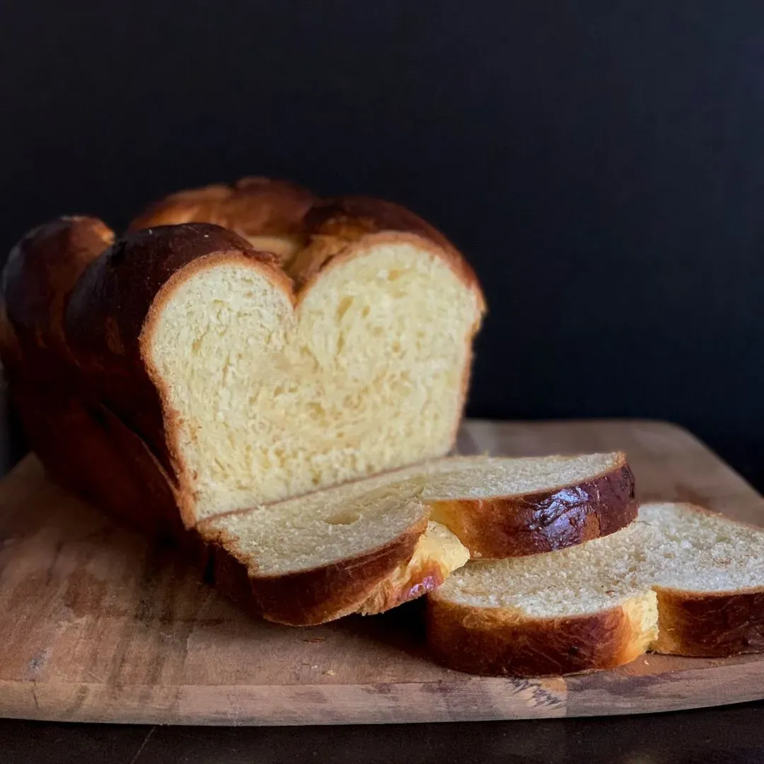 Une brioche posé sur une planche à découper en bois avec deux tranches coupées