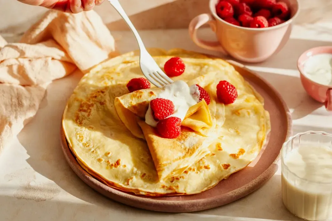 crepes sur une assiette avec des fraises et de la creme chantilly sur le dessus