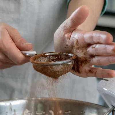 une personne qui saupoudre du cacao avec un tamis