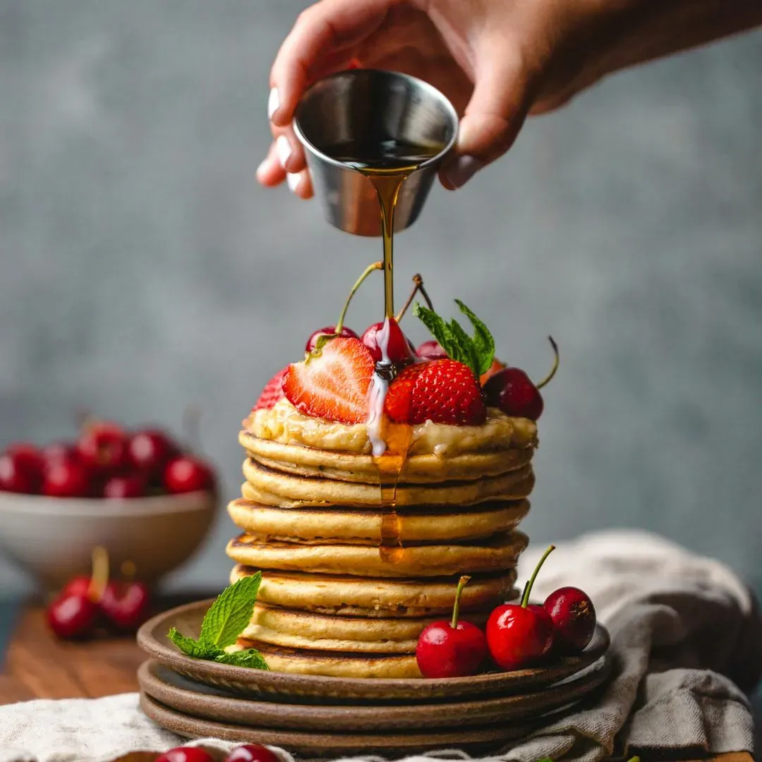 une pile de pancakes sur une assiette et des fraises sur le dessus