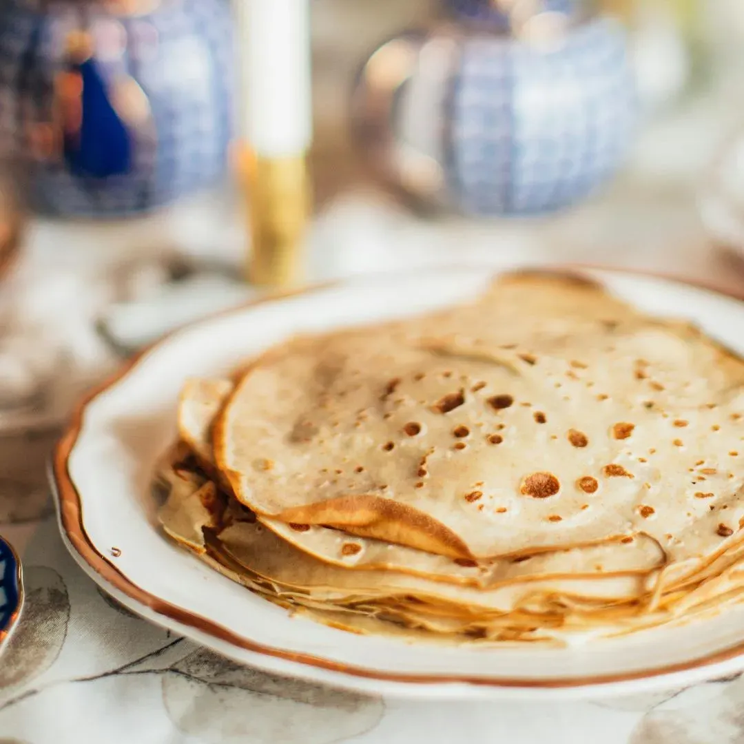 Une pile de crêpe sur une table blanche avec des bougies autour