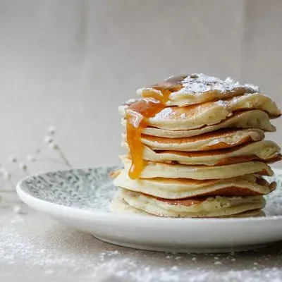 pile de pancakes dorés surmontée de myrtilles fraîches avec du sirop versé dessus