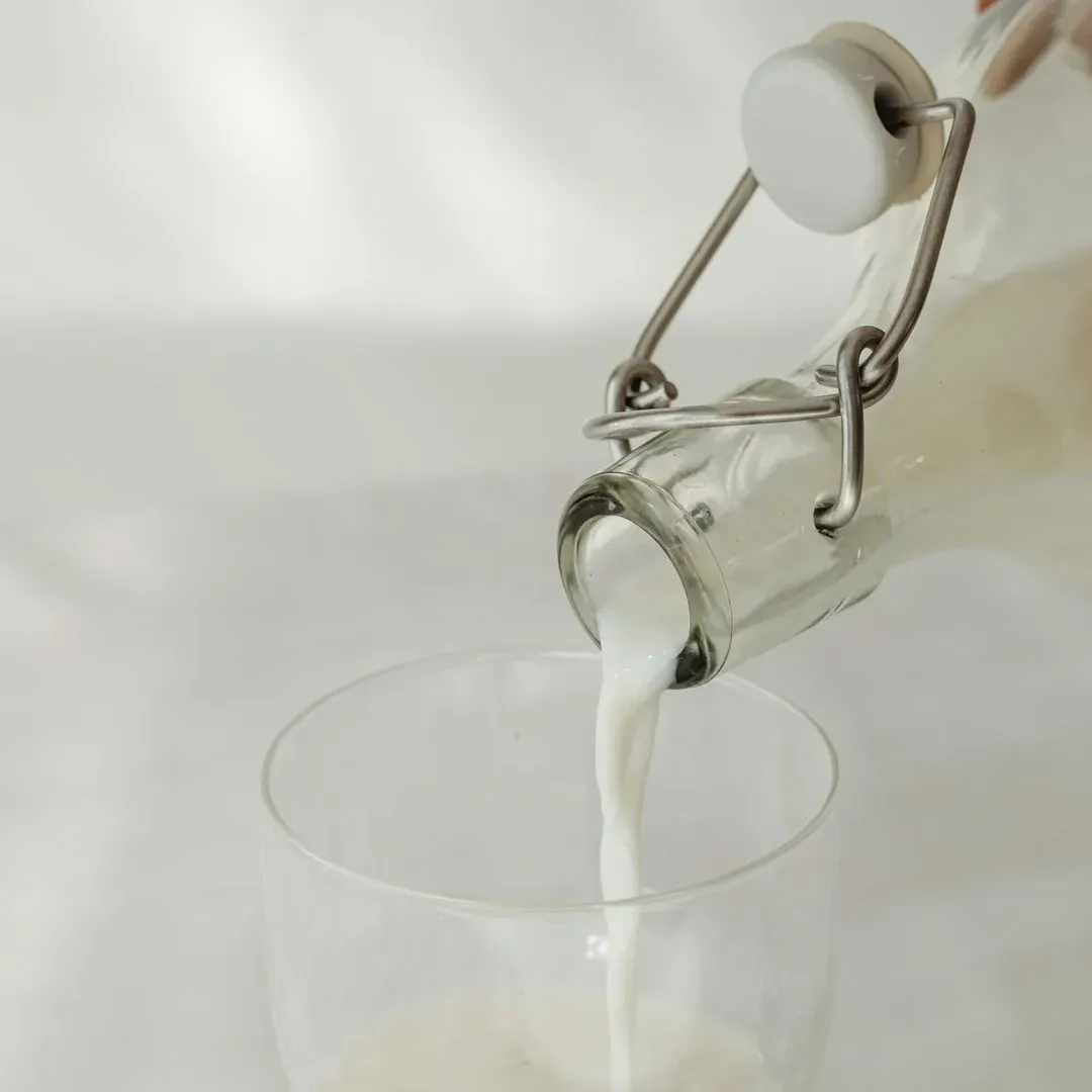 Lait versé d'une bouteille en verre dans un verre transparent sur un fond blanc