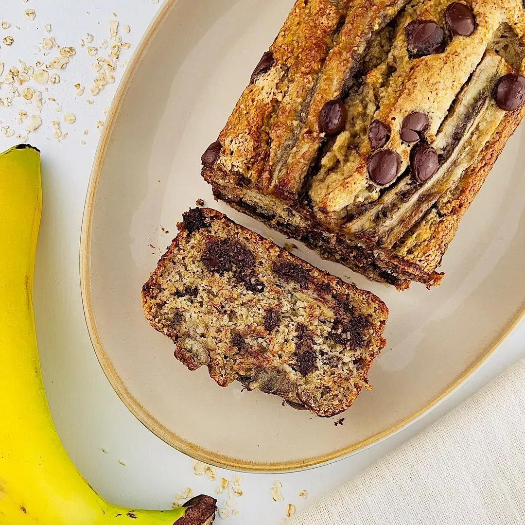 un banana bread aux flocons d'avoine et chocolat sur un plat avec des parts coupées