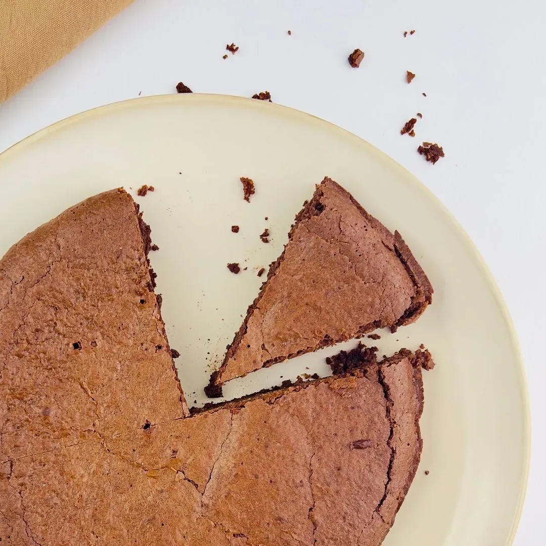 un gateau chocolat et poudre d'amande sur une assiette marron avec une part coupée