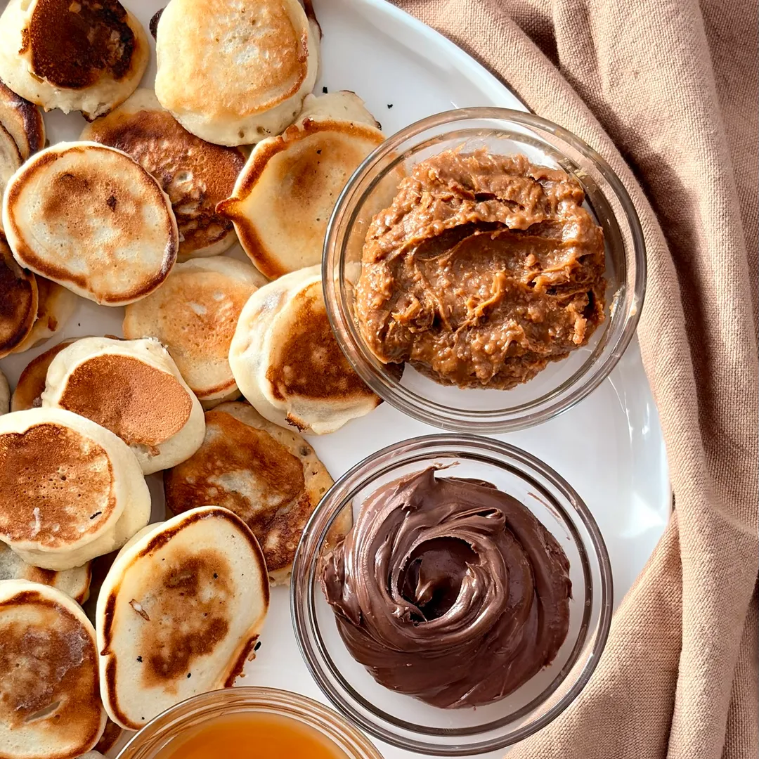 Mini pancakes à la banane des mini pacakes banane avec des petits pot de nutella, miel et pâte de speculoos a côté