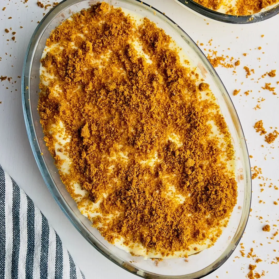 Un tiramisu aux spéculoos saupoudré de miettes de spéculoos, présenté dans un plat ovale en verre.