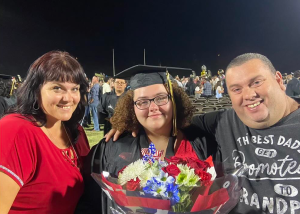 Kat and Marlin celebrating with a graduate holding flowers.