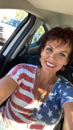 Kat smiling in a car while wearing a red, white, and blue shirt.