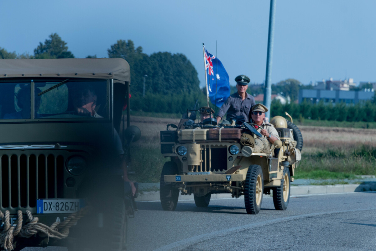 Two Willys jeeps on a suburban road are riding towards the city. One of them has a british flag waving