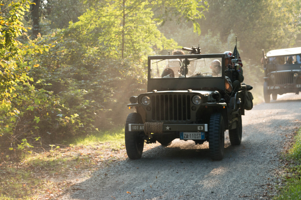Two Willys jeeps cross a cobblestone path in the middle of the woods