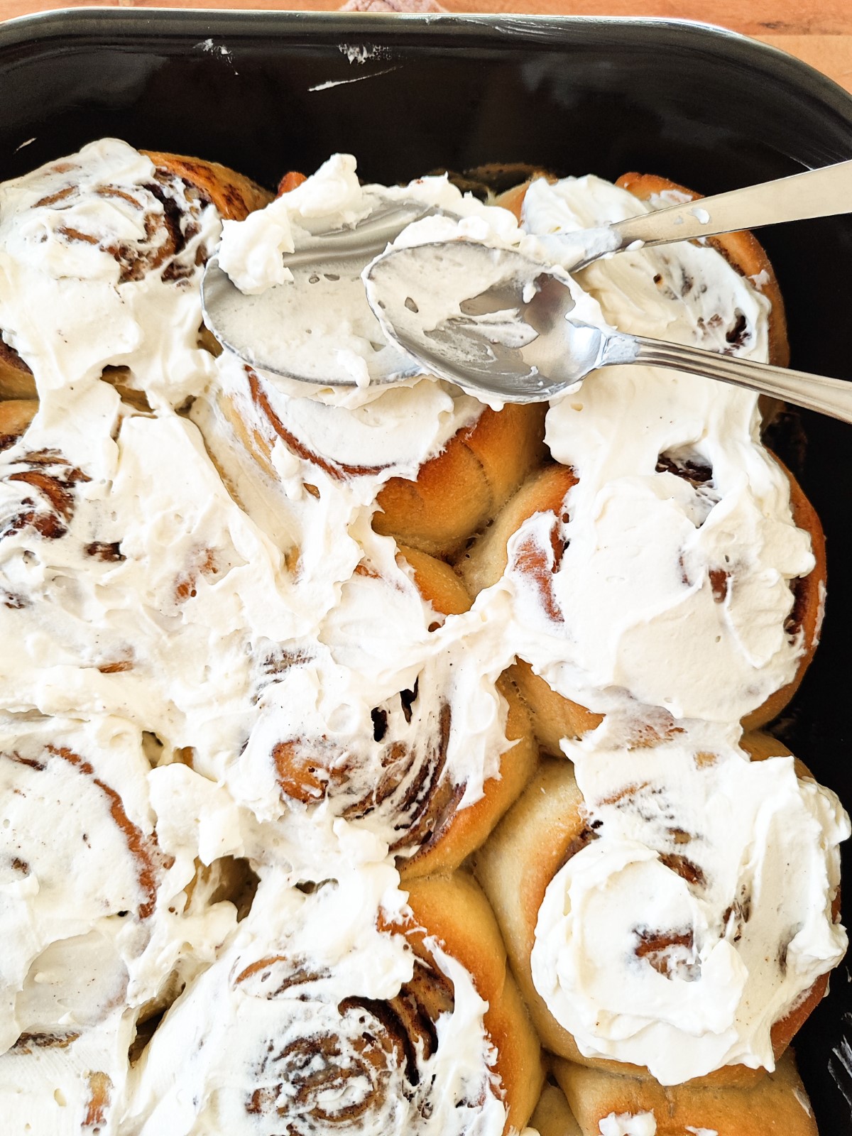 Easy Overnight Cinnamon Rolls - rolls in a black baking tray with cream cheese frosting