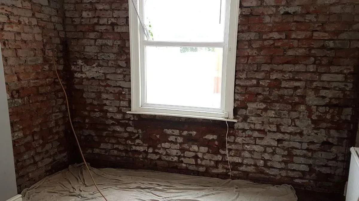 Exposed red brick wall around a window stripped back to bare masonry during a damp proofing and remediation project in Brislington, Bristol.