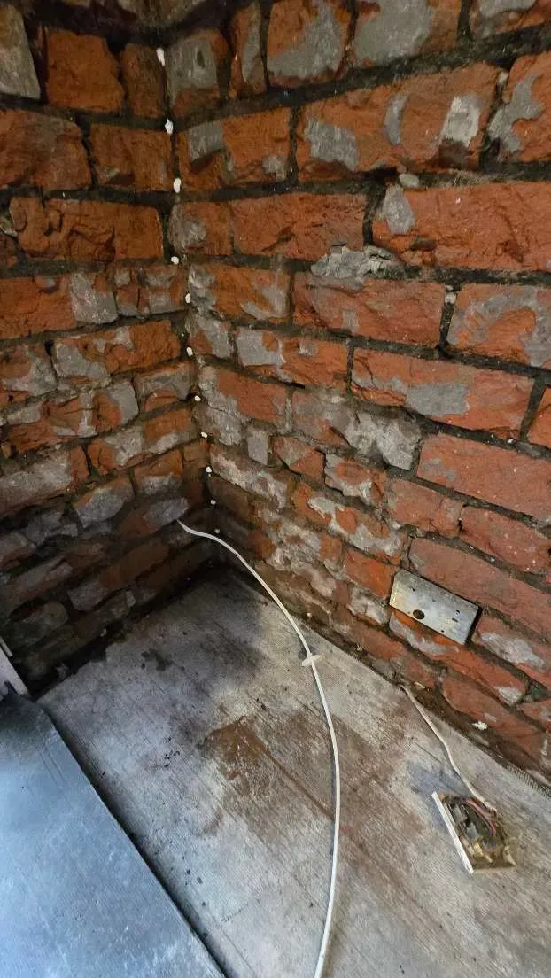 Corner of an internal room stripped to bare red brick with chemical DPC injection holes visible along the mortar course in Brislington.