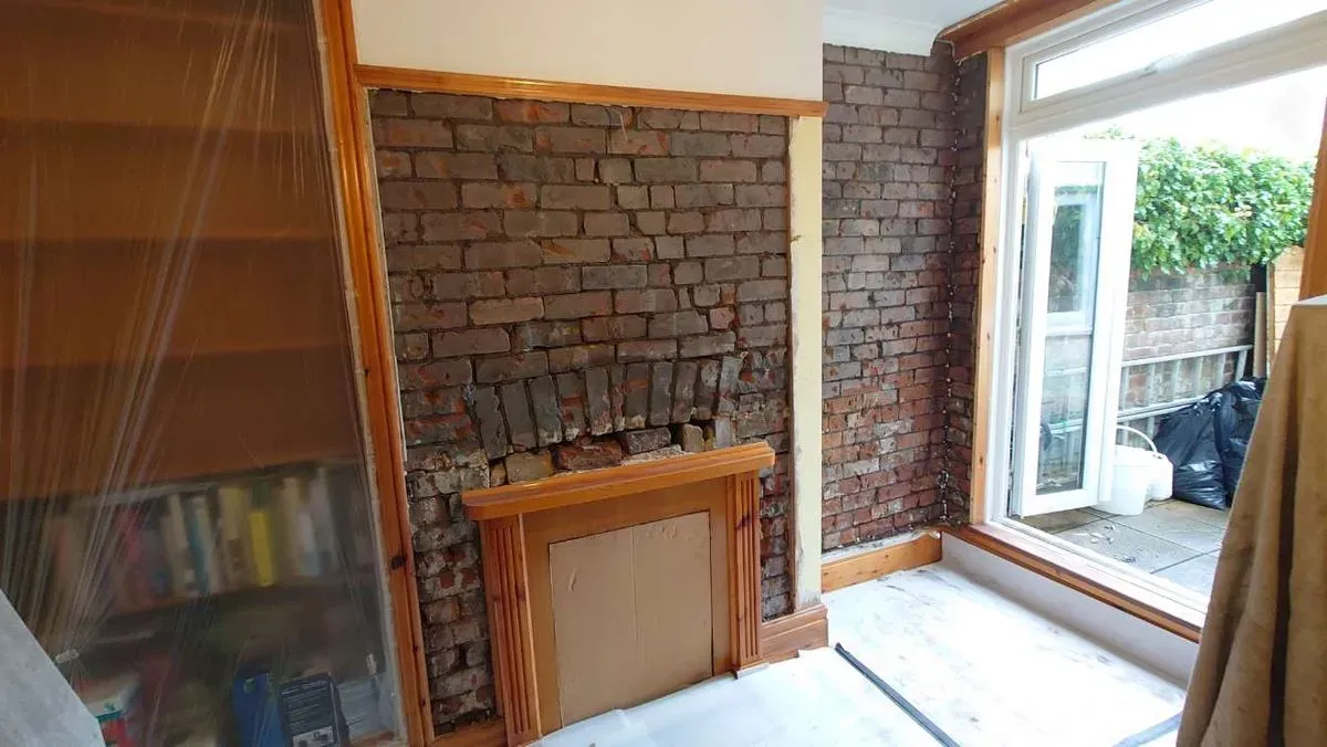 Exposed brick chimney breast and adjacent wall stripped of plaster for damp proofing treatment next to a patio door in Fishponds, Bristol.