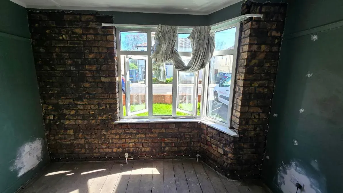 Living room with green walls featuring an external bay window wall stripped to bare brick for a chemical damp proof course (DPC) installation in Henleaze, Bristol.