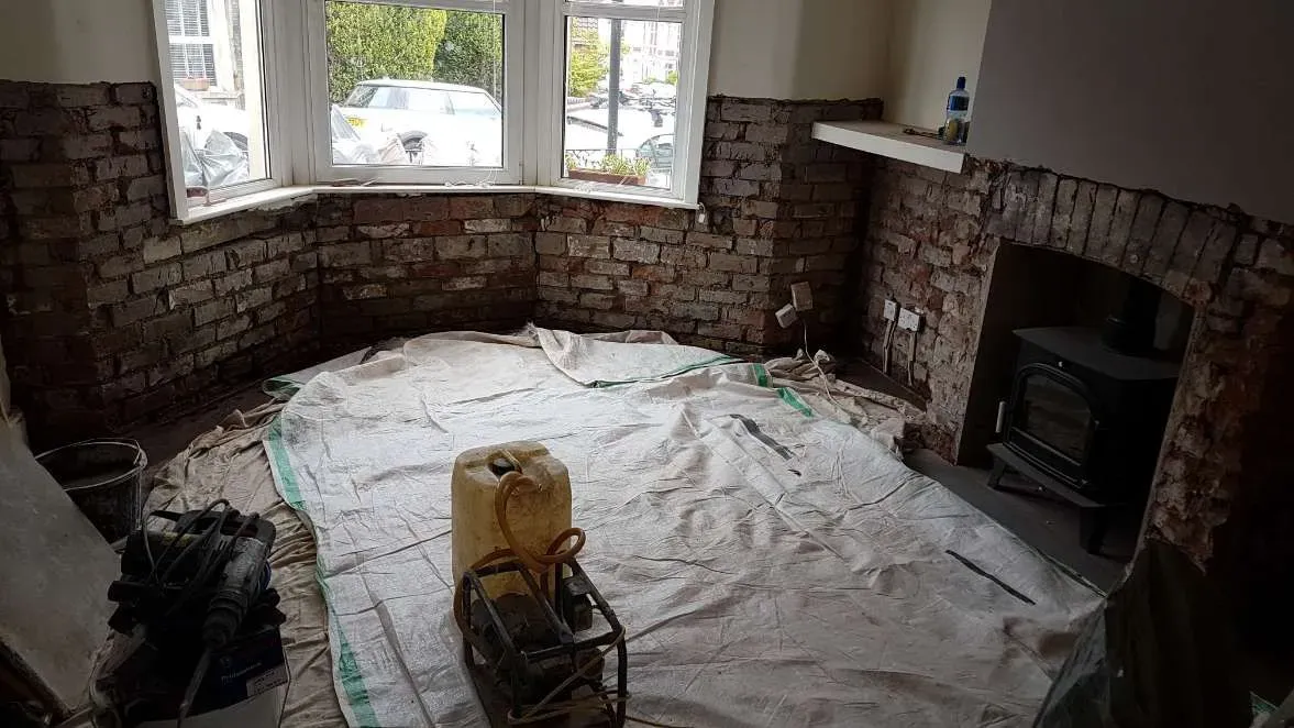 Living room bay window wall stripped back to bare brickwork for professional damp proof course installation in Brislington, Bristol.