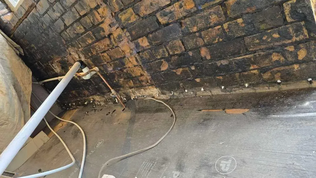 Close-up of damp-proofing cream injected into drilled mortar joints along an exposed brick kitchen wall with plumbing pipes in Henleaze.