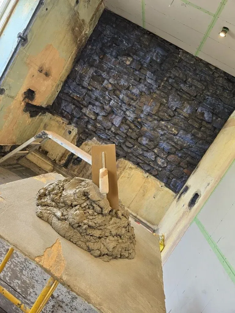 Professional plastering hawk and trowel with wet render mix, prepared for application on a stone wall in a Bristol residential project.