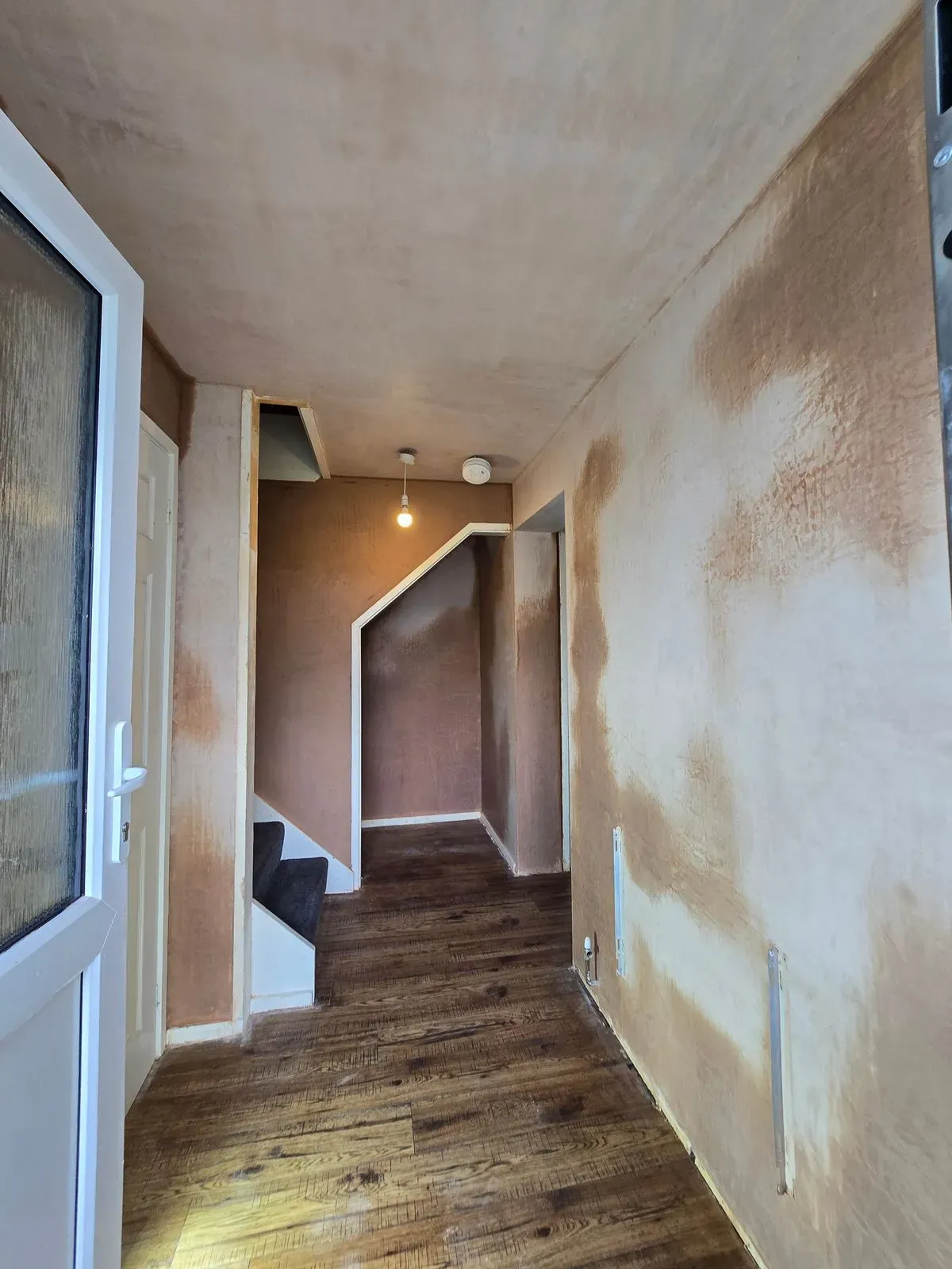 Completed hallway plastering job showing smooth finish near front door and stairs