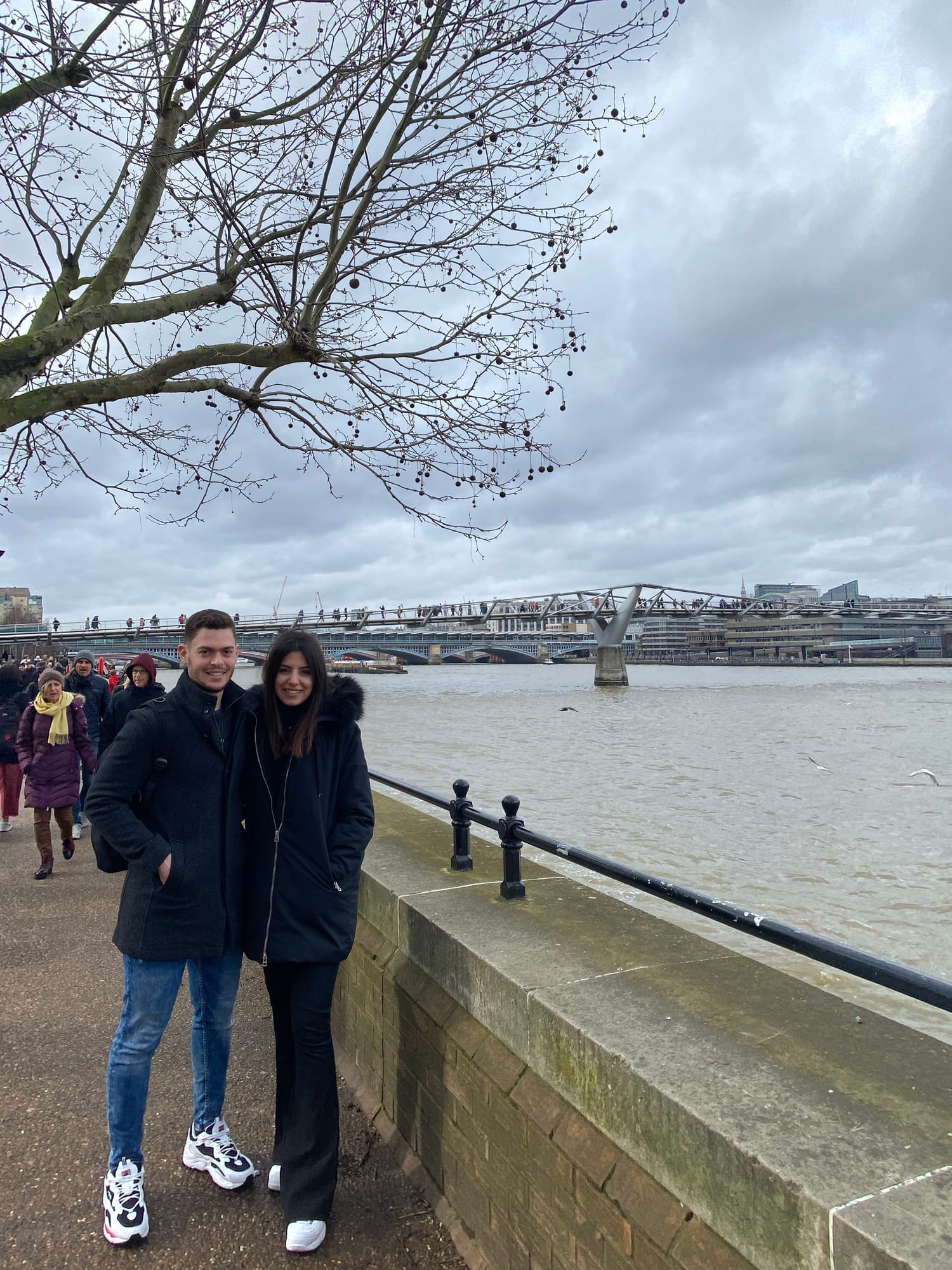 Couple standing together on the Thames embankment in winter coats, Millennium Bridge in the background