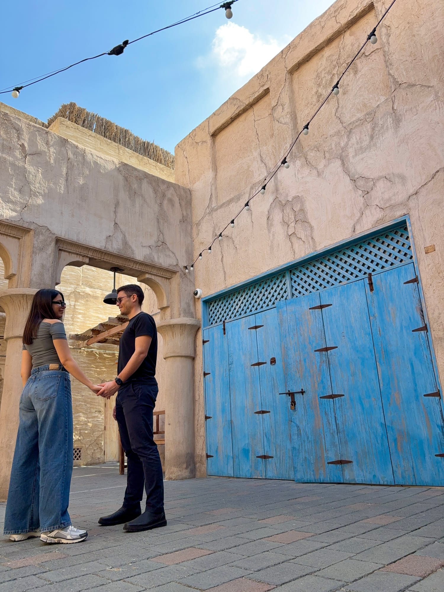 Couple standing facing each other and holding hands in a historic Arabian courtyard with a striking blue door