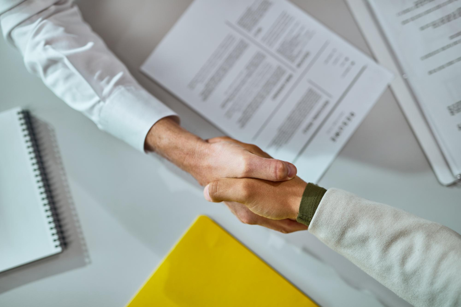 Two people shaking hands with a contract in the background