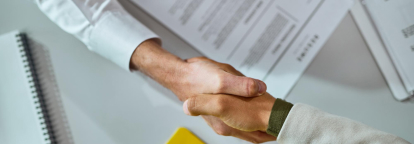 Two people shaking hands with a contract in the background