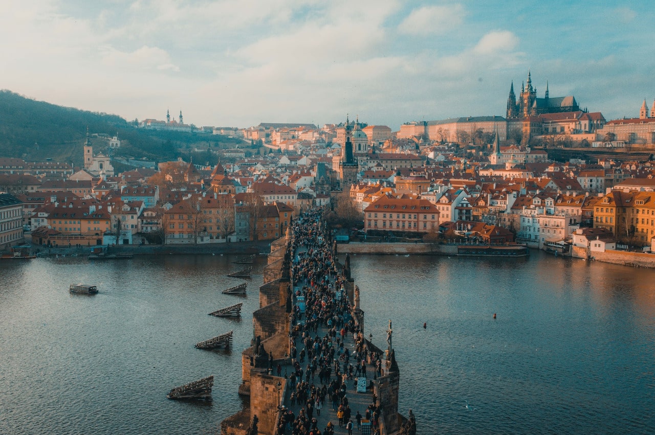 A crowd of pedestrians cross the Charles Bridge over the Vltava River in Prague.