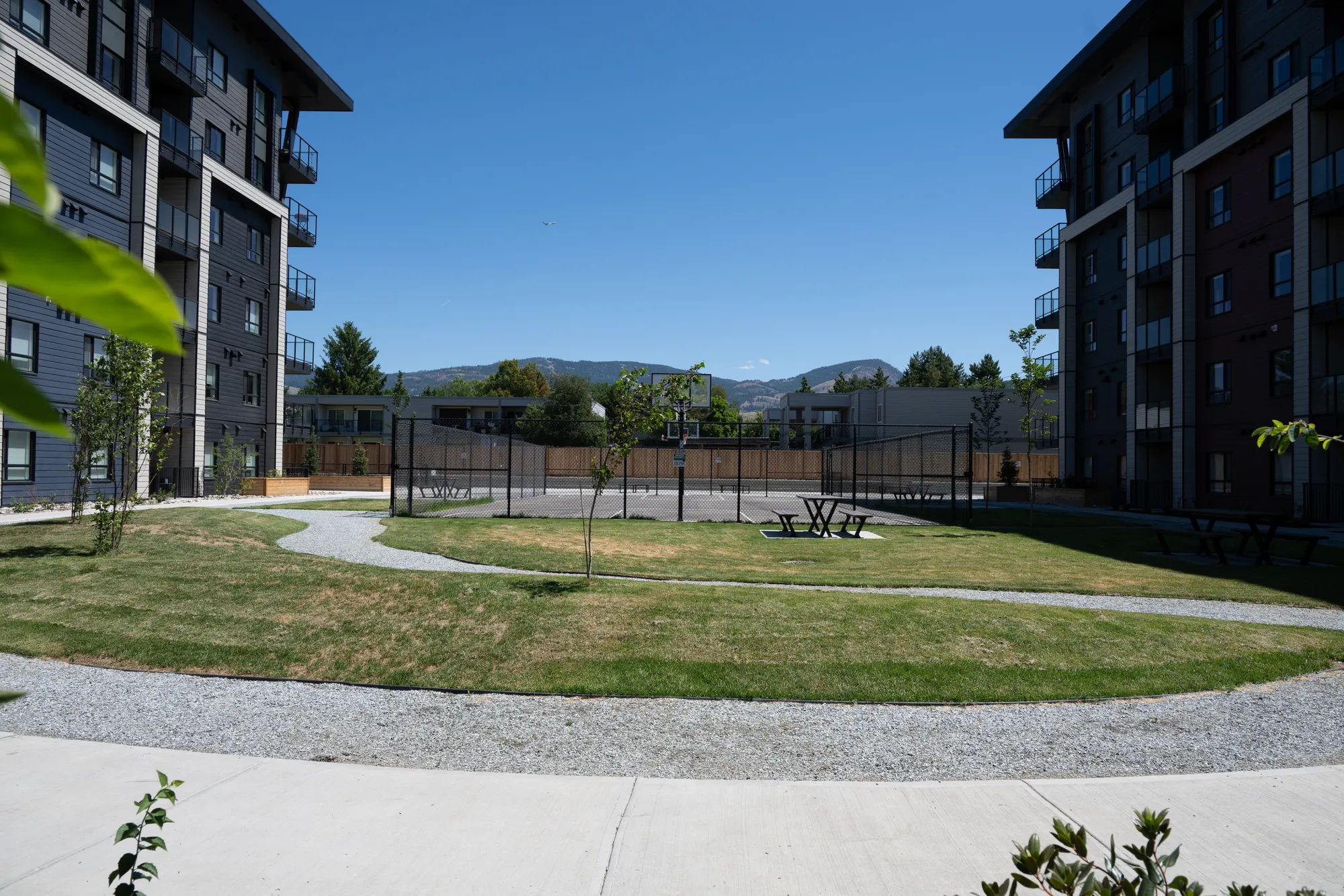 Bayview picnic tables provide seating in a landscaped common area between apartment buildings. The tables offer a place for residents to gather and enjoy the outdoor space.