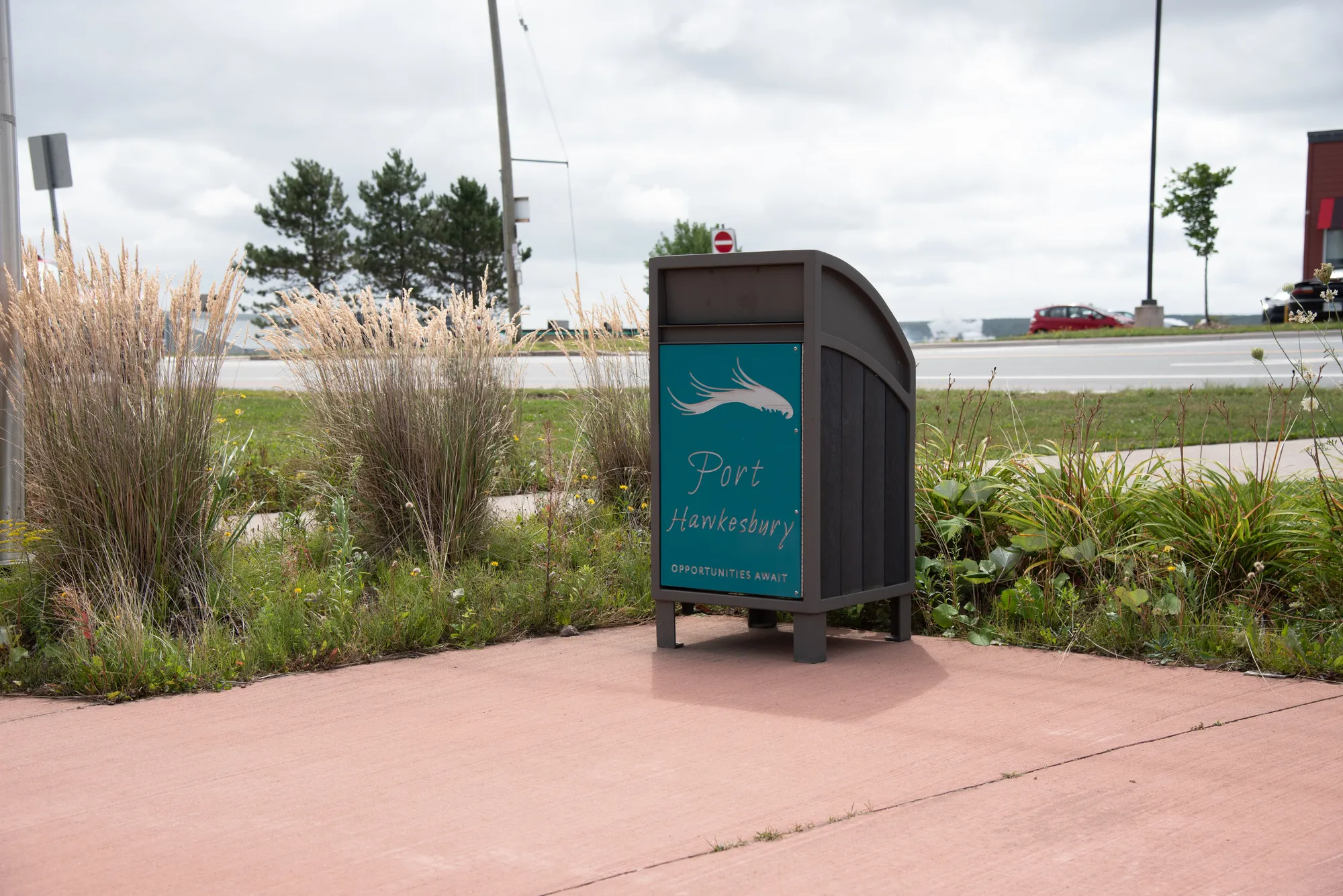 Modena curved top waste receptacle in a public space. The bin features recycled plastic lumber and a powder-coated metal frame.