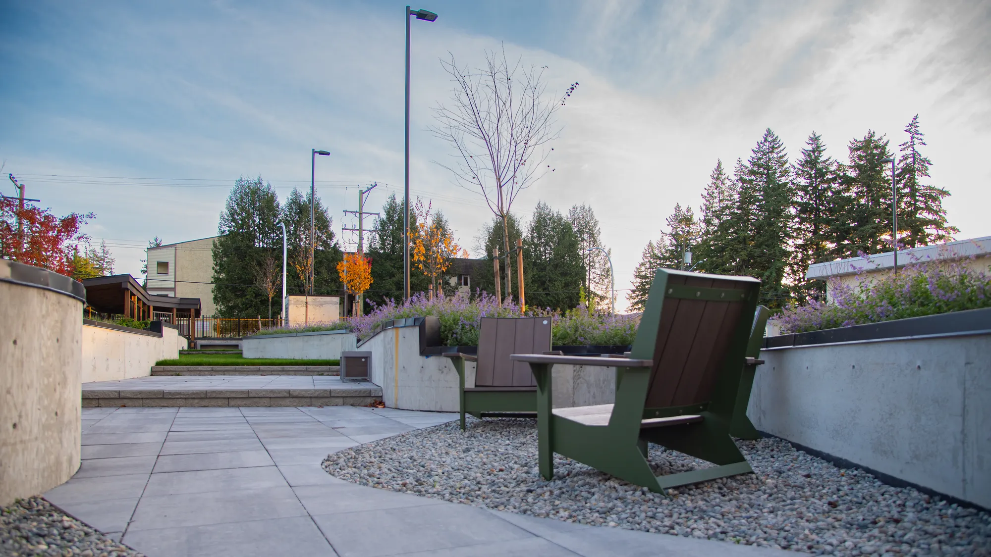 Outdoor lounge area featuring JEM Lounge Chairs in a landscaped setting. The chairs are arranged on a gravel bed, surrounded by concrete planters and greenery.