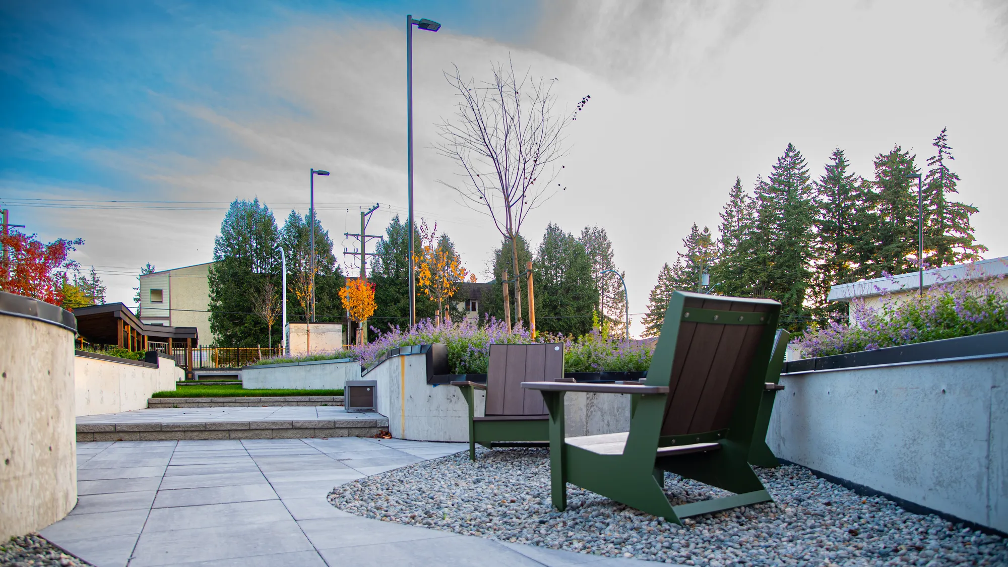 Two lounge chairs provide seating in an outdoor space with concrete planters and landscaping. The chairs feature recycled plastic lumber and powder-coated metal frames.
