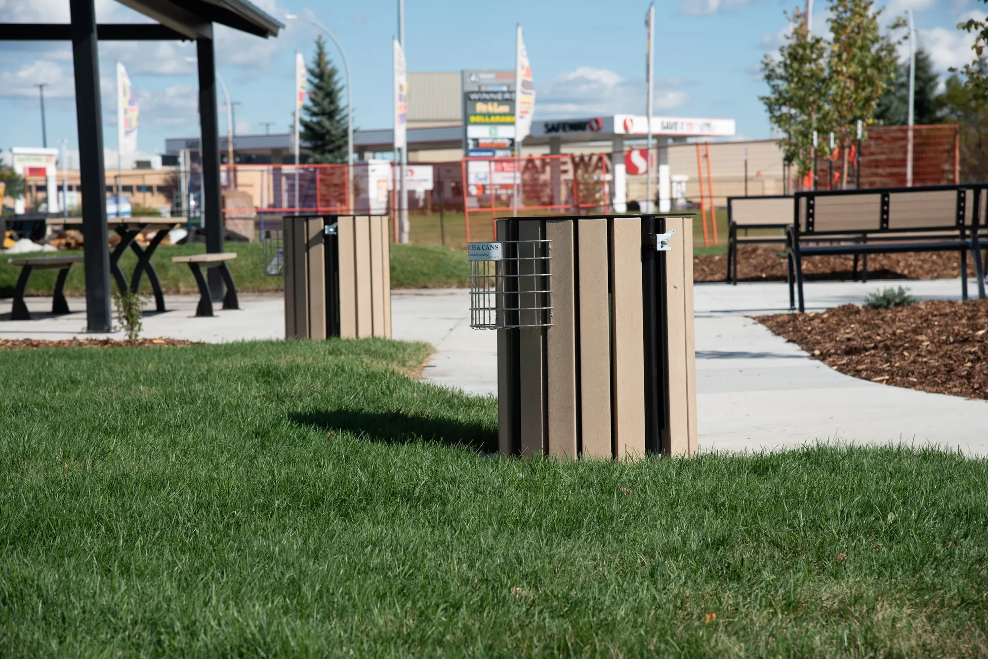 West End waste receptacles with bottle and can recyclers are placed in a park setting. These durable bins help keep public spaces clean and promote recycling.