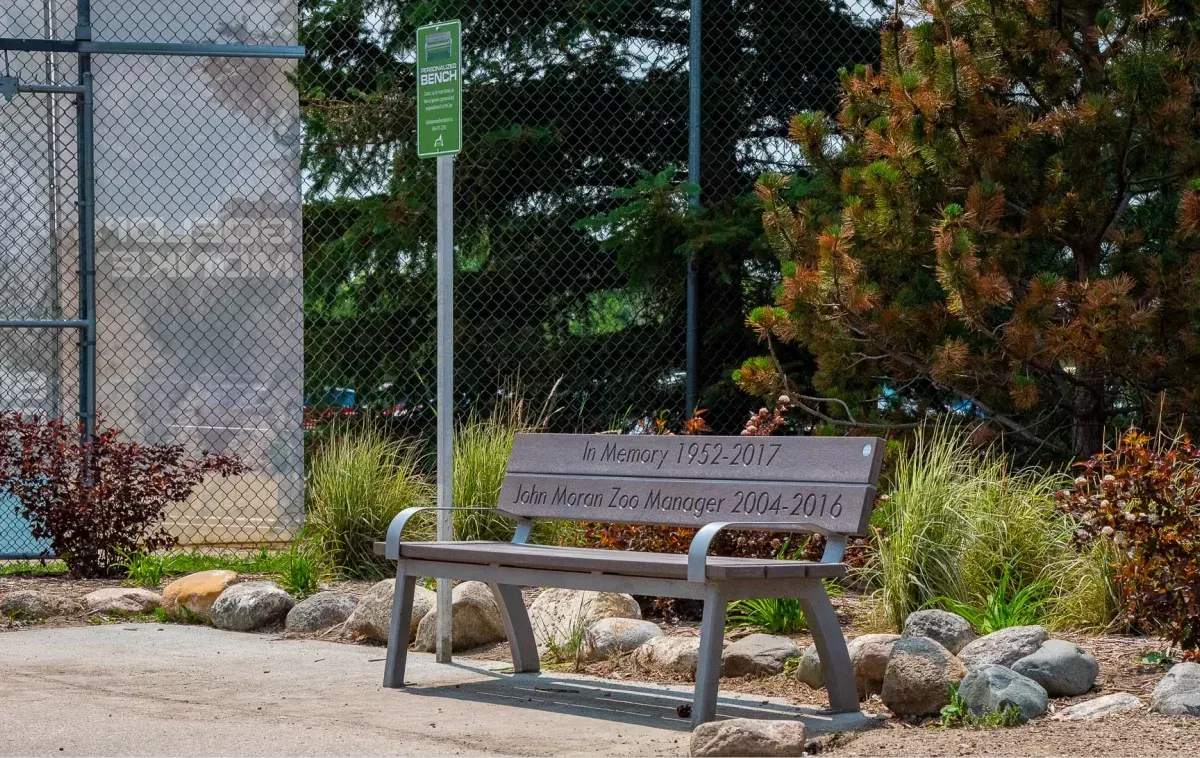 A memorial Aylesbury bench is installed at the Saskatoon Forestry Farm Park and Zoo. The bench features recycled plastic lumber and a metal frame.
