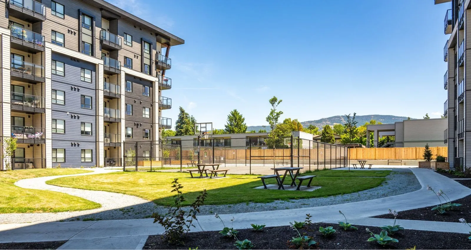 Outdoor picnic tables provide seating in a grassy courtyard between apartment buildings. The tables offer a place for residents to gather and enjoy the outdoor space.