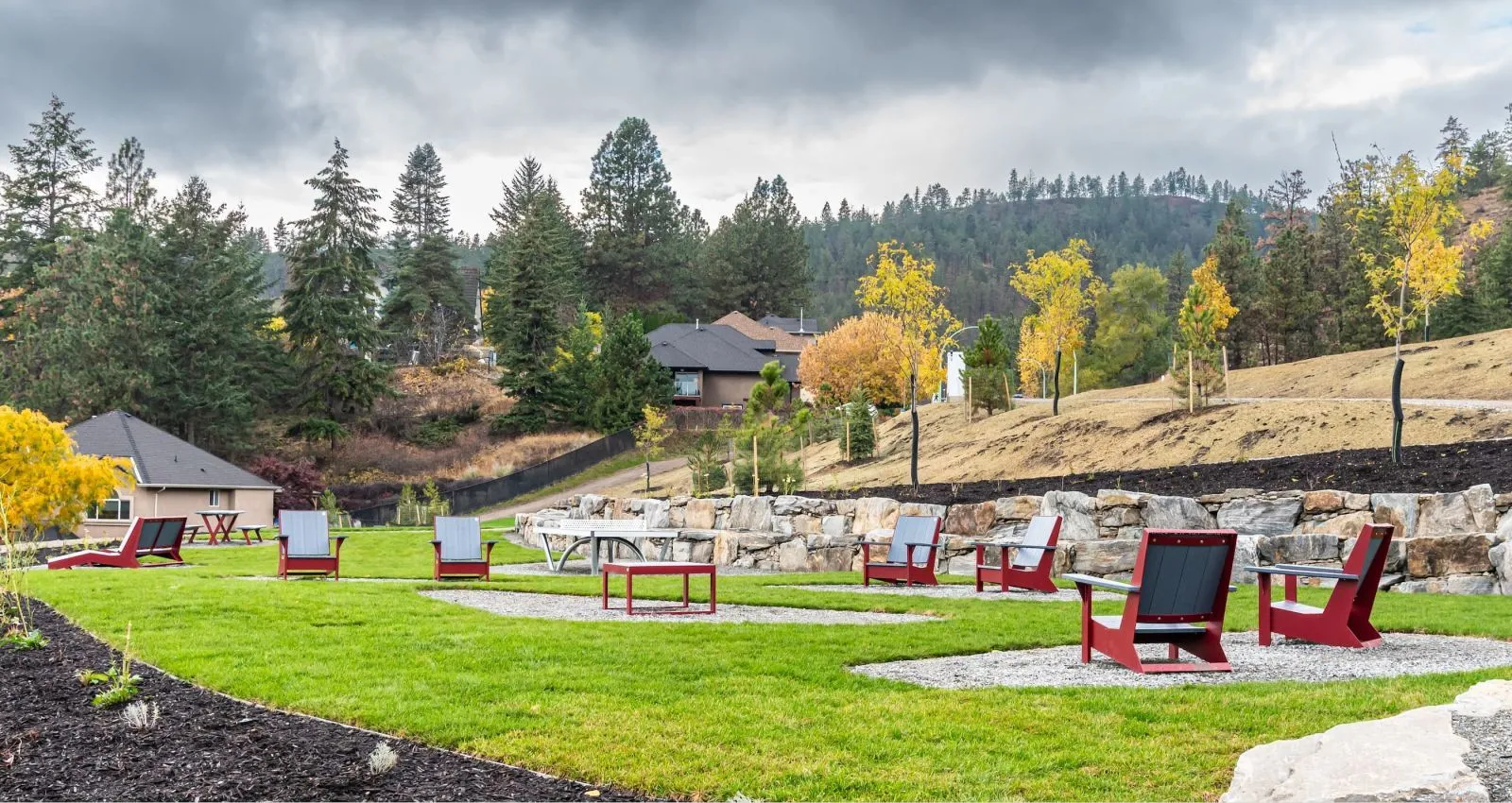 Outdoor lounge area featuring Jem Lounge Chairs and Side Tables arranged on gravel pads within a grassy park setting. The site furniture provides a relaxing space amidst the natural landscape.