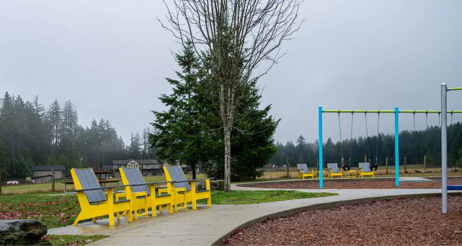 Bright yellow lounge chairs provide a comfortable seating option along a paved path in Meadow Drive Community Park. The chairs offer a place to relax and enjoy the park's natural surroundings.