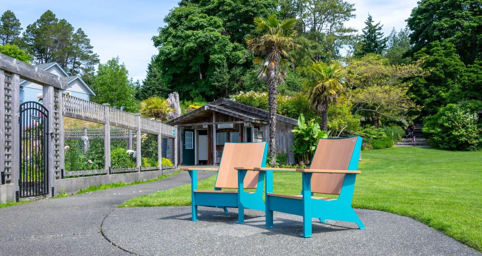 Two JEM Lounge Chairs provide comfortable seating in a lush park setting. The chairs feature recycled plastic lumber and powder-coated metal frames.