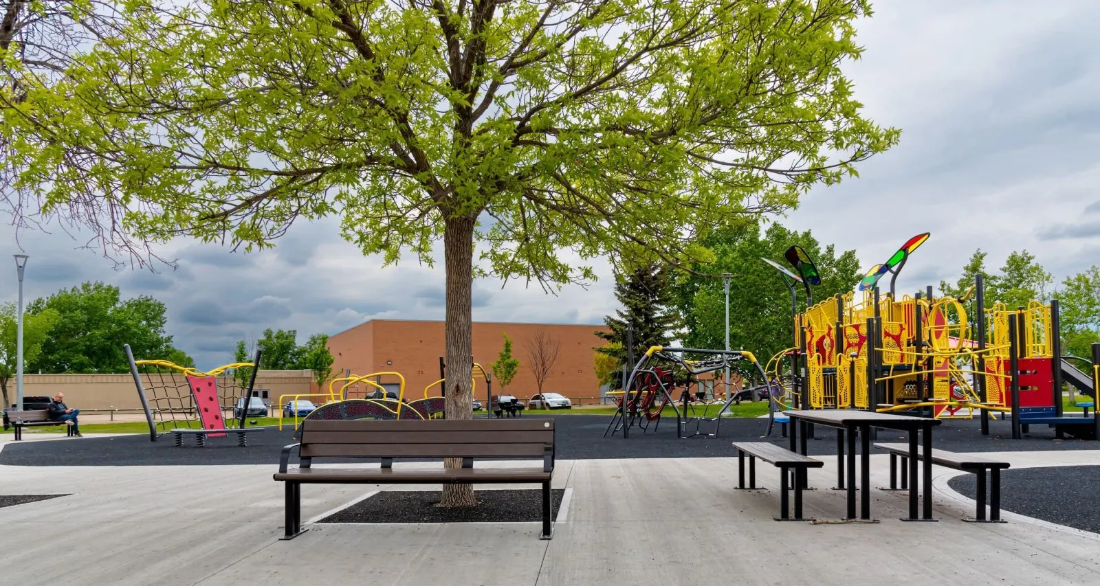 Outdoor setting featuring a Larson Picnic Table and Larson Bench, providing seating in a recreational area. The site furniture complements the playground and green space.