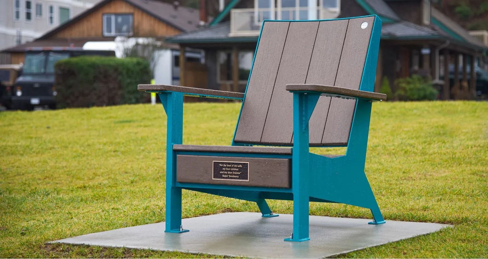 A JEM Lounge Chair provides comfortable outdoor seating. The chair features brown recycled plastic lumber and a teal powder-coated frame, set on a concrete pad in a grassy area.