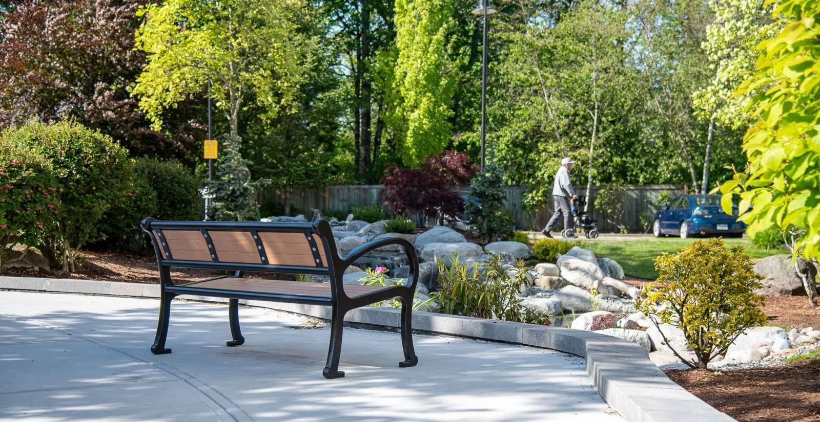 A Mountain Classic bench offers seating in a landscaped park setting. The bench features recycled plastic lumber slats and a black powder-coated frame.