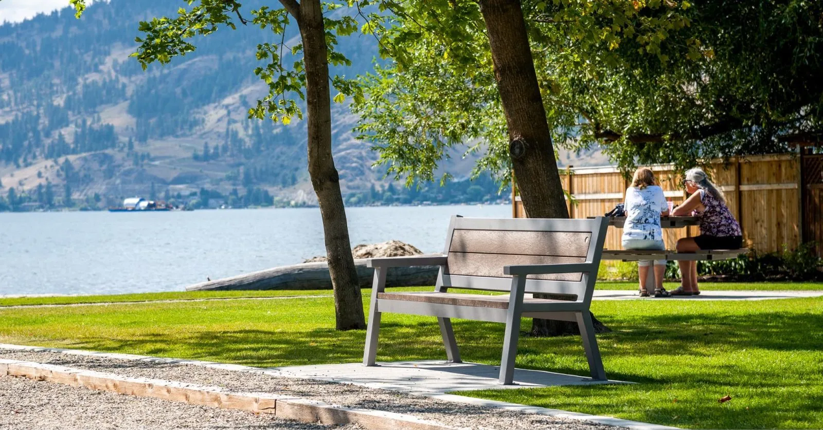 The Rutherford Angled Leg Bench provides comfortable seating in a lakeside park setting. The bench features recycled plastic lumber and a powder-coated metal frame.
