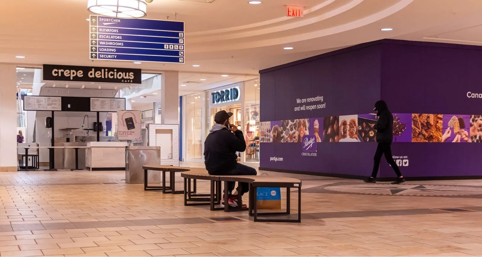 Curved benches provide seating in a shopping mall. The benches feature a dark metal frame and light-colored recycled plastic lumber.